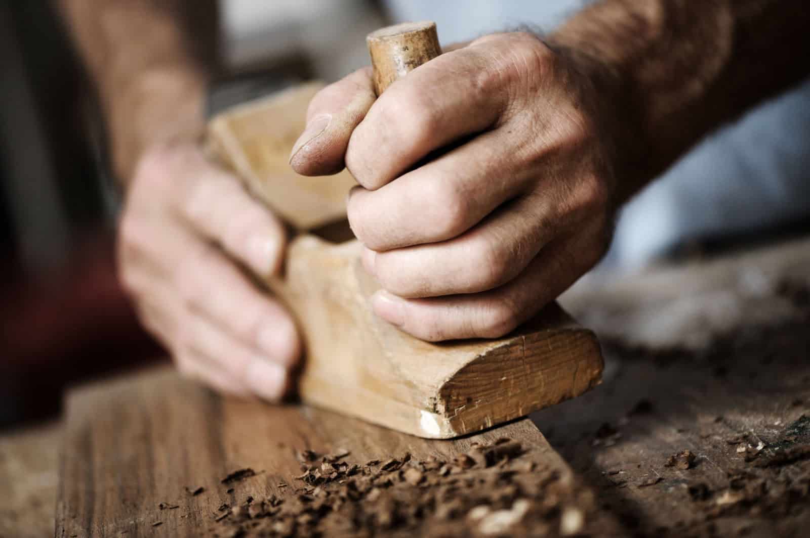 hands of a carpenter planing a plank of wood with a hand plane